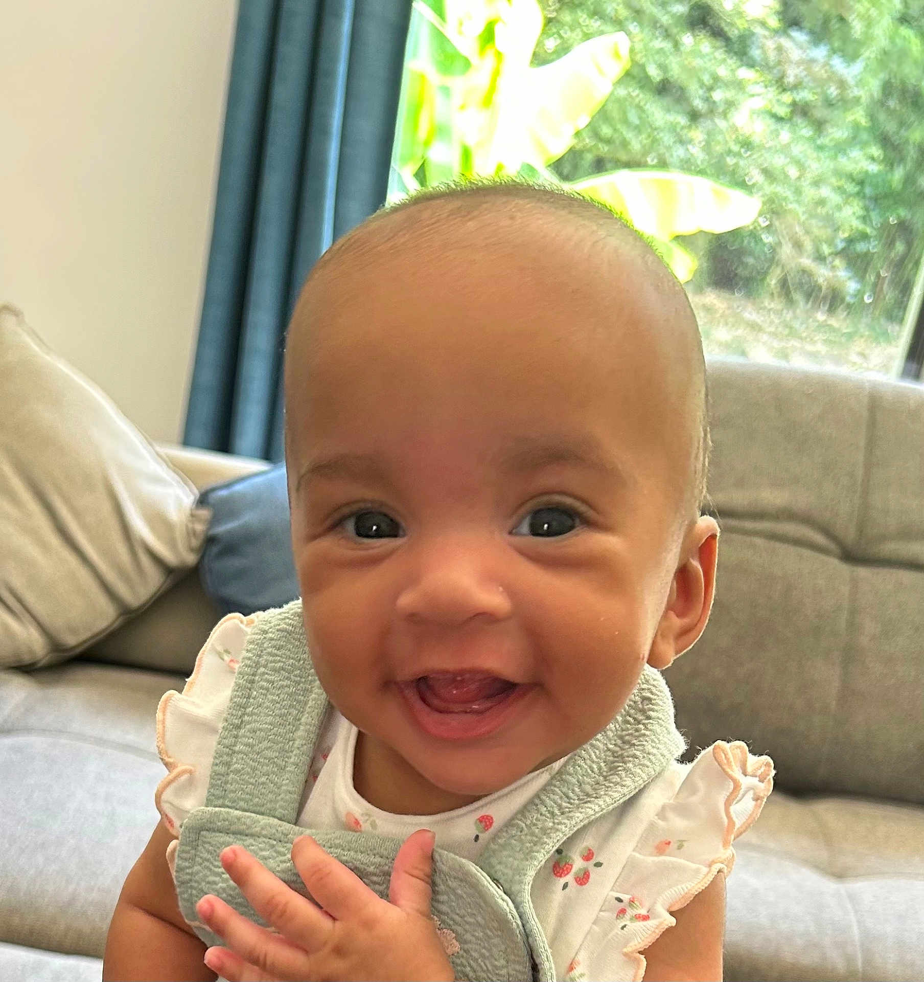 Eva participe au concours pour gagner de l'argent avec cette photo : baby, smiling, face, child, indoor, couch, pillow, clothing, person, happy, cute, infant, furniture, window, curtain, greenery, hand, eyes, portrait, ruffled_sleeves