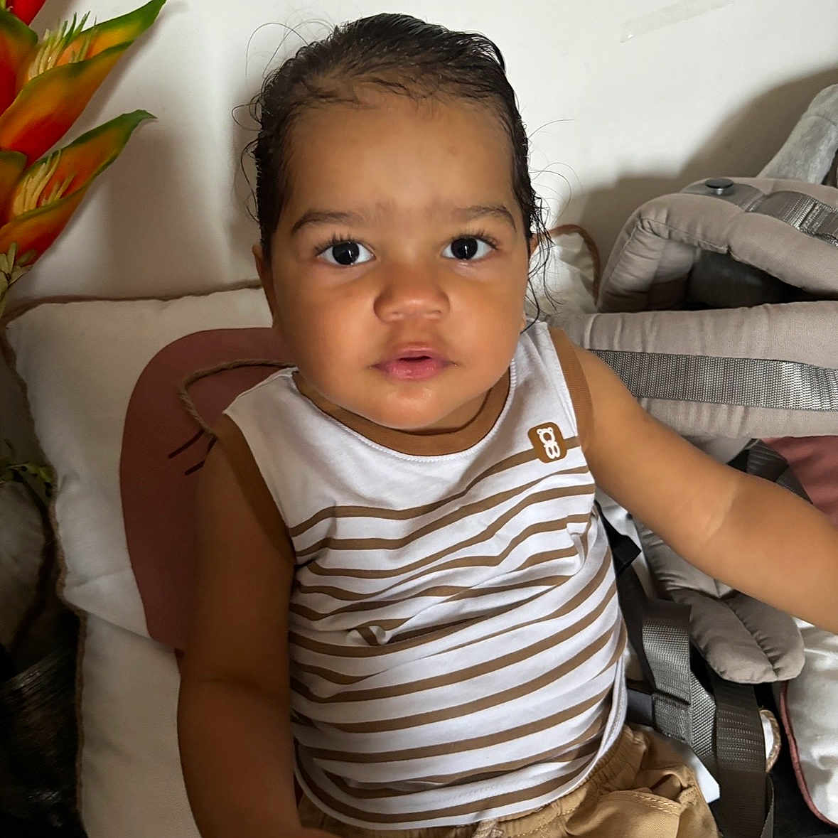 Nahe participe au concours pour gagner de l'argent avec cette photo : baby_carrier, brown_shorts, casual_clothing, child, curly_hair, cushion, cute, expression, face, flower_decoration, home_interior, indoor, looking_at_camera, person, pillow, portrait, sitting, striped_clothing, toddler, young_child