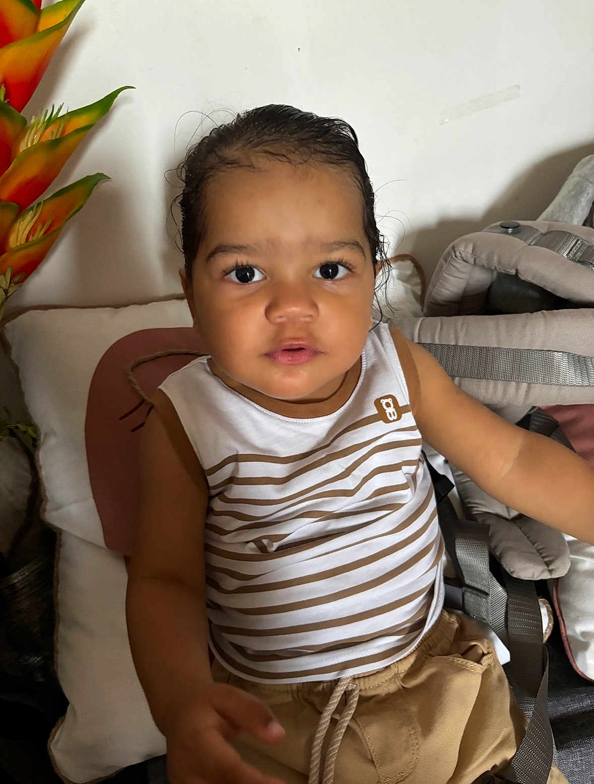 Nahe participe au concours pour gagner de l'argent avec cette photo : toddler, child, portrait, indoor, striped_clothing, sitting, cushion, baby_carrier, pillow, curly_hair, brown_shorts, face, looking_at_camera, expression, young_child, casual_clothing, home_interior, flower_decoration, person, cute