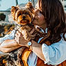 woman, dog, yorkshire_terrier, pet, outdoor, sunlight, affection, holding, watch, white_shirt, orange_vest, portrait, smiling, hair, face, cute, animal, companion, nature, background_blur