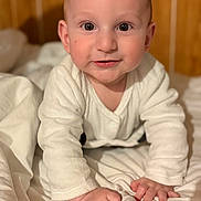 Tiago a rejoint le concours — aidez-le/la à gagner de superbes lots ! baby, child, infant, crawling, white_clothing, blanket, bed, wooden_wall, indoors, cute, smile, face, hands, eyes, skin, portrait, young, soft_lighting, expression, person