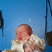 Sophia is registered to the contest to win money with this photo: baby, newborn, infant, clothing, onesie, hand, face, expression, blue_wall, indoor, person, child, cute, sleepy, fingers, room, bag, pattern, soft, young