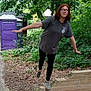 Hailey is registered to the contest to win money with this photo: person, young_person, glasses, red_hair, balancing, wooden_beam, outdoor, park, greenery, trees, pathway, portable_toilet, purple, casual_clothing, tshirt, leggings, shoes, nature, summer, daytime