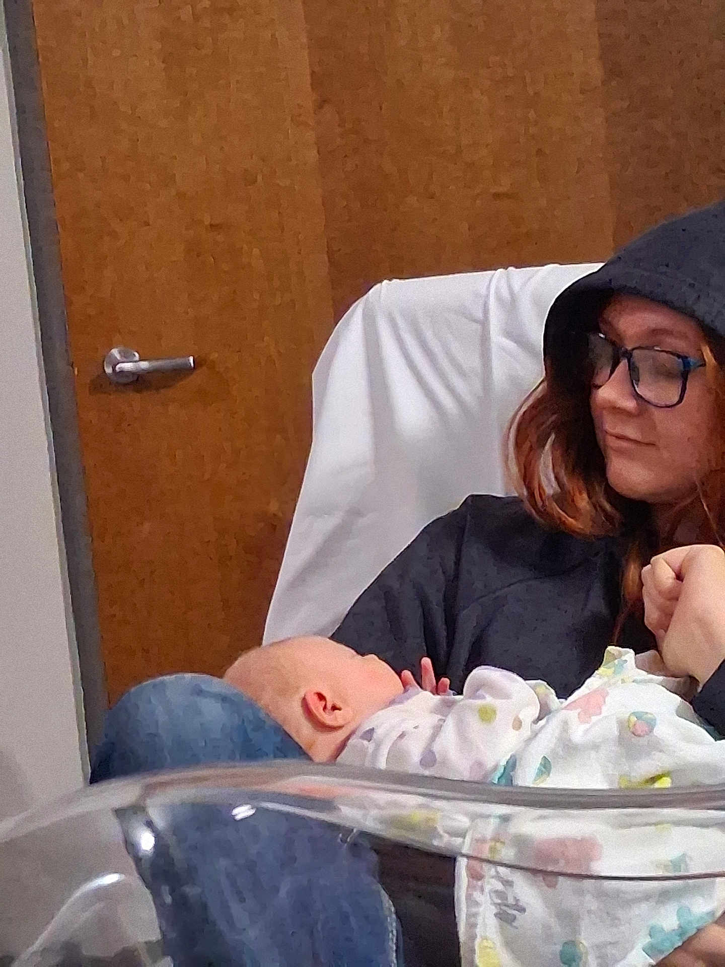 Hailey is registered to the contest to win money with this photo: baby, person, glasses, hoodie, indoor, door, wood, blanket, seated, caring, infant, holding, comfort, casual, portrait, resting, warmth, love, human, parenting