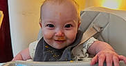 James is registered to the contest to win money with this photo: baby, high_chair, food, messy, bib, smile, face, child, indoor, light, hand, table, cute, fun, happy, infant, feeding, clothing, person, portrait