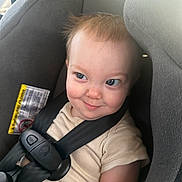 James is registered to the contest to win money with this photo: toddler, car_seat, child, seatbelt, smile, face, hair, clothing, safety, infant, baby, seat, straps, cute, indoors, person, young_child, expression, cheeky, playful