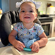 Gema joined the competition — help win amazing prizes! baby, blue_outfit, bow, child, curly_hair, cute, food_area, happy, headband, high_chair, indoor, kitchen, person, playful, portrait, smile, table, toddler, toy, young_child