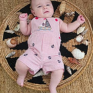 Isaac is registered to the contest to win money with this photo: baby, infant, child, romper, striped_clothing, nautical_theme, seashells, woven_mat, floor, curious_expression, raised_fists, cute, portrait, lying_down, indoors, soft_lighting, skin, person, head, legs