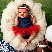 Lilith is registered to the contest to win money with this photo: baby, infant, newborn, headband, tutu, red_tutu, football, football_helmet, pom_poms, cheer_poms, plush_bed, fluffy_bed, football_field, artificial_turf, stadium, portrait, adorable, hands_up, bare_feet, props