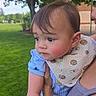 Aiden is registered to the contest to win money with this photo: adult_arm, baby, bib, blue_clothing, child, curious, daylight, face, grass, green, holding, nature, outdoor, park, person, portrait, skin, sunny, tree, young_child