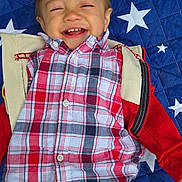 Aiden is registered to the contest to win money with this photo: toddler, child, smiling, laughing, portrait, lying_down, plaid_shirt, red_jacket, blue_blanket, stars, outdoor_style, happy, face, head, clothing, infant, playful, close_up, photography, family