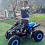 child, boy, smile, quad_bike, atv, toy, gloves, hoodie, sneakers, grass, backyard, playhouse, trees, wheels, mud, outdoor, portrait, toy_car, sportswear, young_child
