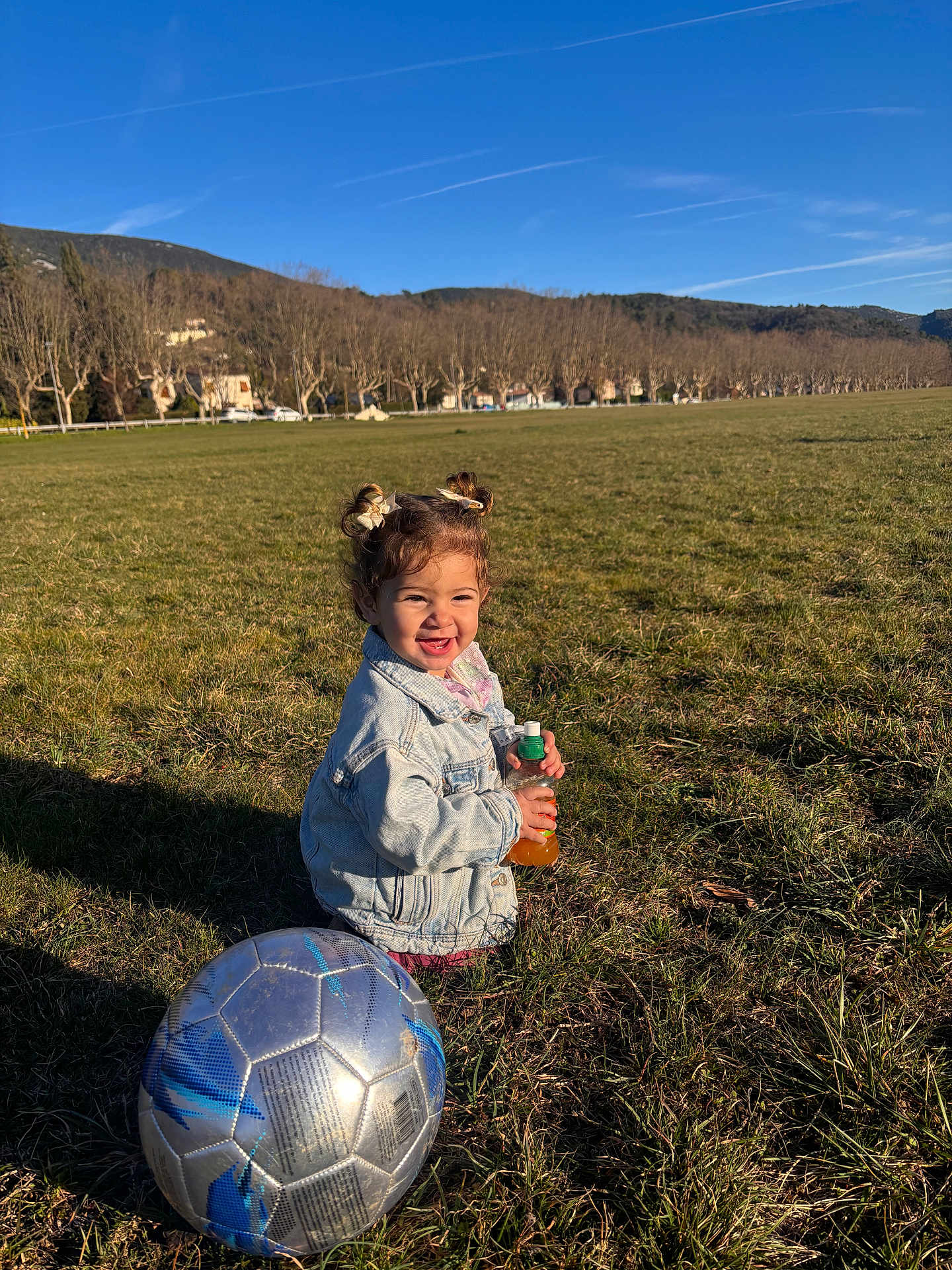 Inaya participe au concours pour gagner de l'argent avec cette photo : child, toddler, smile, soccer_ball, juice_bottle, jean_jacket, pigtails, grass, field, outdoors, park, sunny, shadow, play, happy, recreation, nature, portrait, toy, weekend