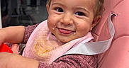 Inaya a rejoint le concours — aidez-le/la à gagner de superbes lots ! arm, baby, bib, closeup, curly_hair, dark_background, feeding_time, food, happy, highchair, indoor, infant, messy_face, pink_seat, red_bowl, reflection, rosy_cheeks, sleeve, smile, tongue_out