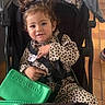 baby, casual_clothing, child, curly_hair, cute, floor_tiles, footwear, green_purse, happy, indoor, leopard_print, person, pigtails, portrait, seated, smiling, straps, stroller, toddler, young_child