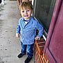 child, boy, smiling, blue_checkered_shirt, jeans, black_shoes, porch, brick_wall, window, sidewalk, casual_pose, outdoor, daylight, happy, person, young, short_hair, hand_on_hip, concrete, home_exterior