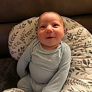 Denny is registered to the contest to win money with this photo: baby, infant, smiling, blue_clothing, cushion, patterned_fabric, seated, happy, face, head, indoor, soft_lighting, cozy, person, child, onesie, cute, comfort, young, portrait