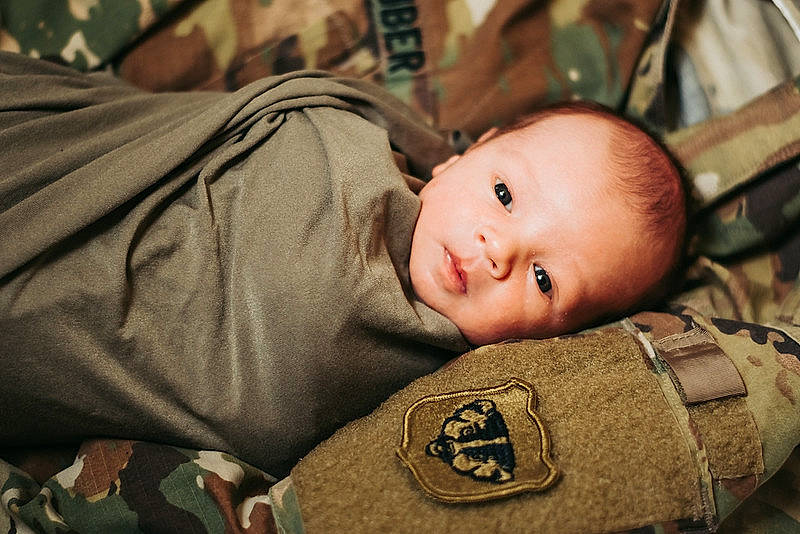 Emmitt is registered to the contest to win money with this photo: baby, baby_products, baby_toddler_clothing, brown, camouflage, cheek, child, comfort, eye, flash_photography, linens, military_camouflage, military_person, military_uniform, pattern, person, sitting, smile, toddler, tree