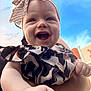 baby, smiling, child, headband, bow, outdoor, sky, blue_sky, patterned_clothing, arm, person, happy, infant, portrait, cute, daylight, building, holding, closeup, skin