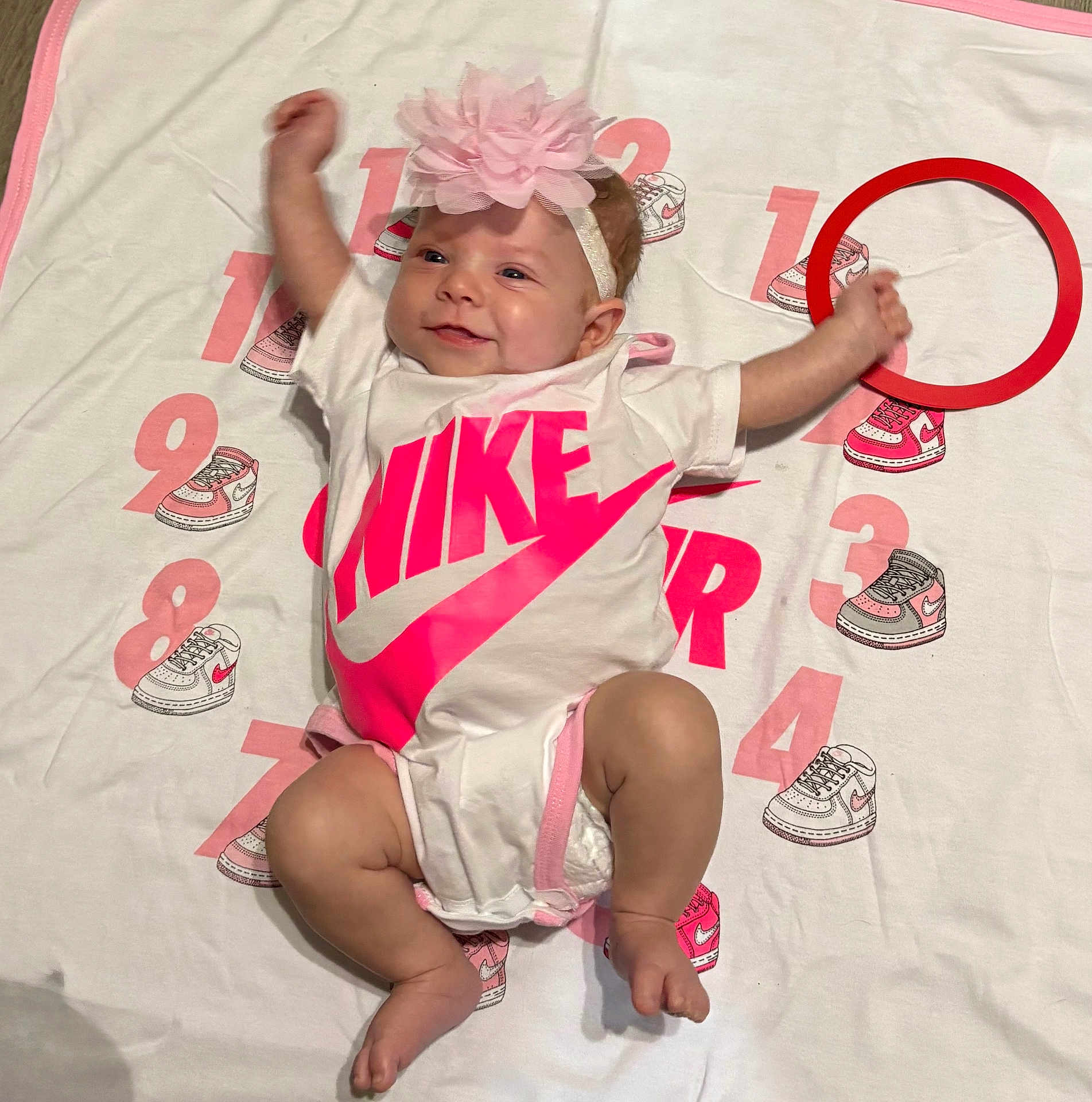 Raelynn Grace is registered to the contest to win money with this photo: baby, infant, headband, flower, onesie, nike, milestone_blanket, numbers, sneakers, pink, white, happy, smiling, arms_up, legs_bent, cute, laying_down, child, indoor, portrait