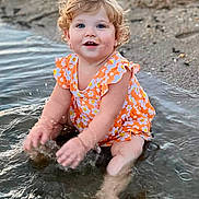Raelynn Grace joined the competition — help win amazing prizes! toddler, child, water, splashing, beach, sand, curly_hair, orange_clothing, floral_pattern, happy, smiling, blue_eyes, summer, outdoor, nature, playful, sitting, cute, fun, daylight