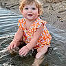 toddler, child, water, splashing, beach, sand, curly_hair, orange_clothing, floral_pattern, happy, smiling, blue_eyes, summer, outdoor, nature, playful, sitting, cute, fun, daylight