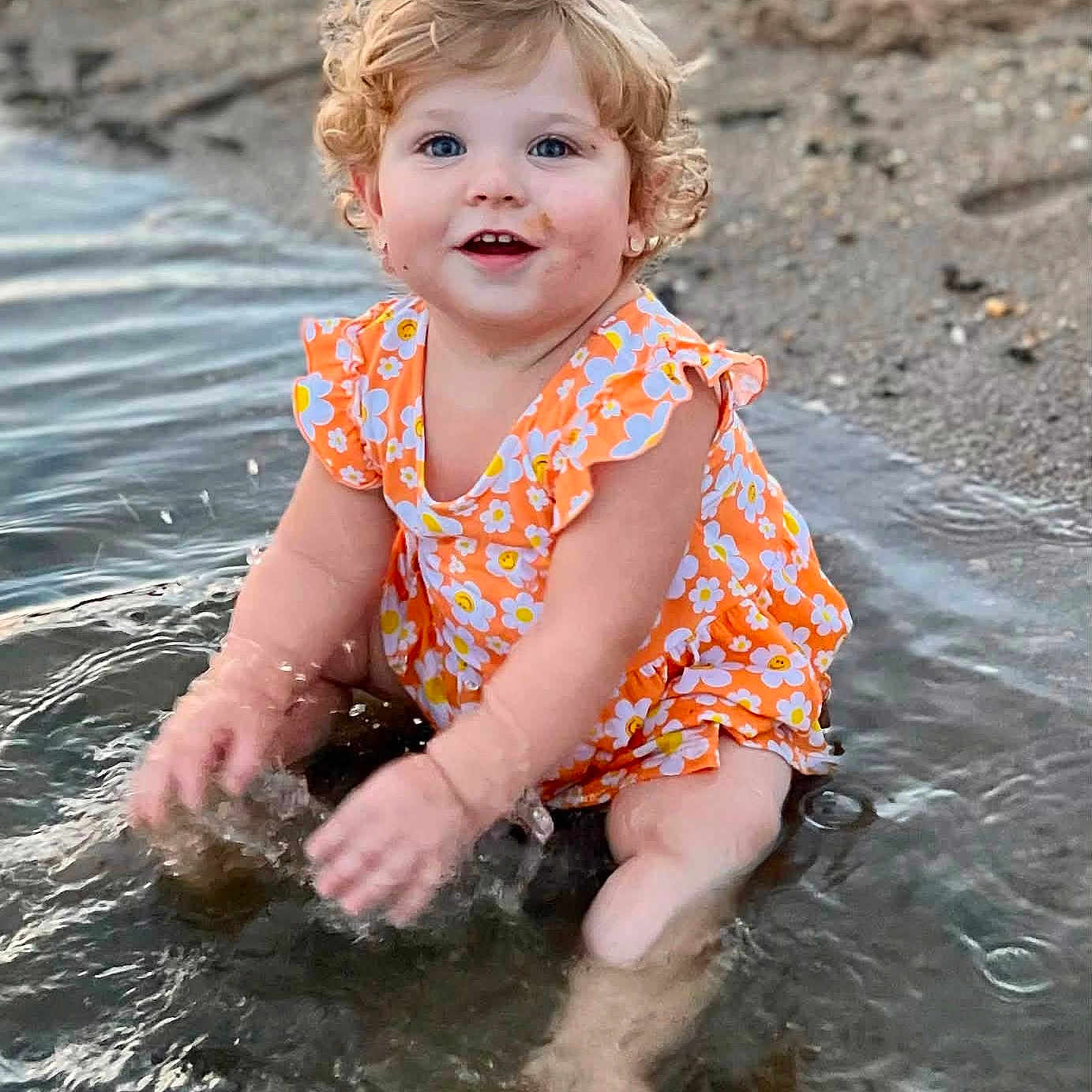 Raelynn Grace joined the competition — help win amazing prizes! toddler, child, water, splashing, beach, sand, curly_hair, orange_clothing, floral_pattern, happy, smiling, blue_eyes, summer, outdoor, nature, playful, sitting, cute, fun, daylight