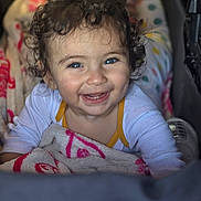 Joud a rejoint le concours — aidez-le/la à gagner de superbes lots ! child, baby, toddler, smiling, curly_hair, blue_eyes, blanket, stroller, onesie, teeth, joyful, portrait, close_up, indoor, bokeh, candid, polka_dots, baby_bottle, hand, blanket_pattern