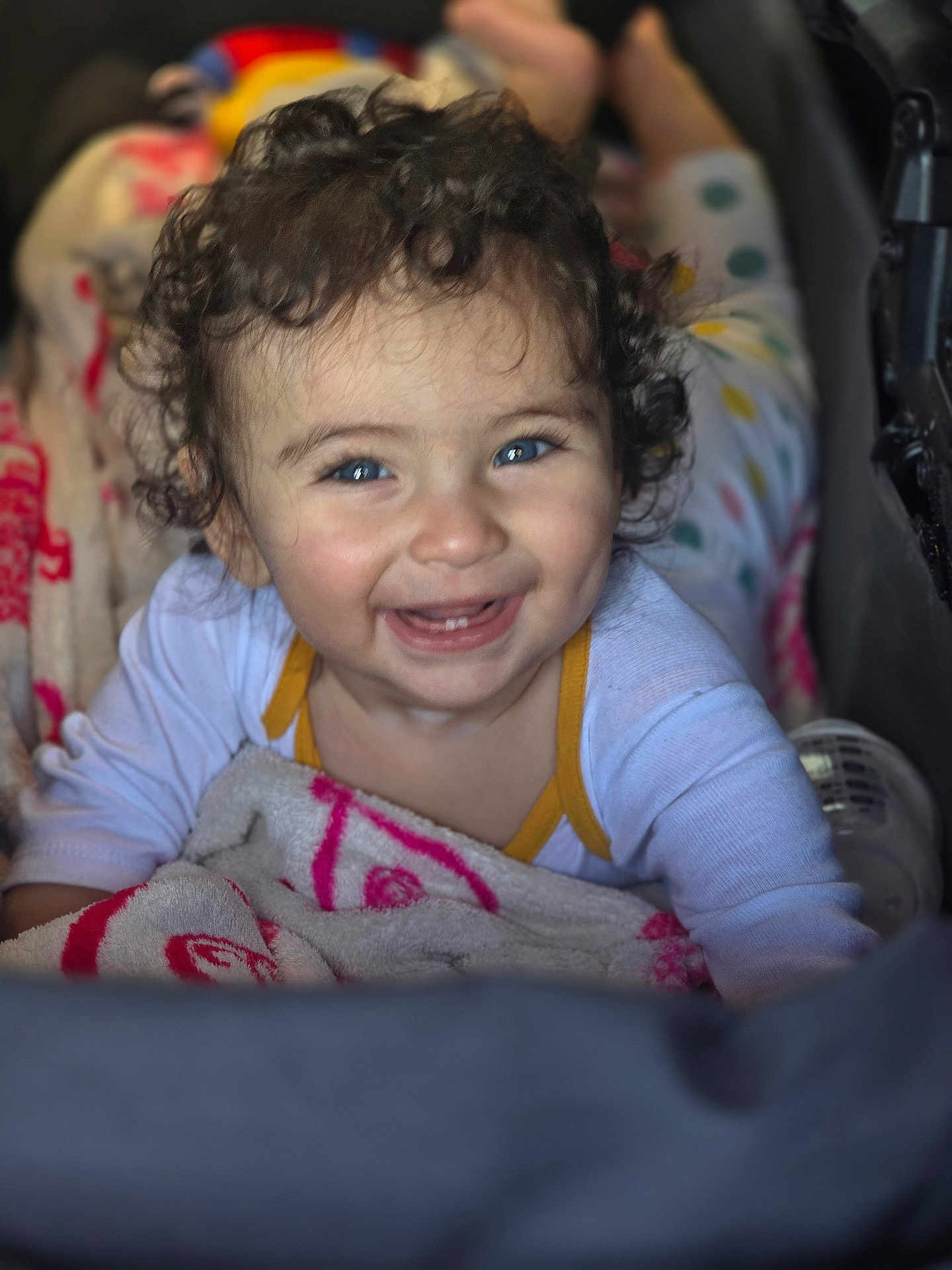 Joud a rejoint le concours — aidez-le/la à gagner de superbes lots ! child, baby, toddler, smiling, curly_hair, blue_eyes, blanket, stroller, onesie, teeth, joyful, portrait, close_up, indoor, bokeh, candid, polka_dots, baby_bottle, hand, blanket_pattern
