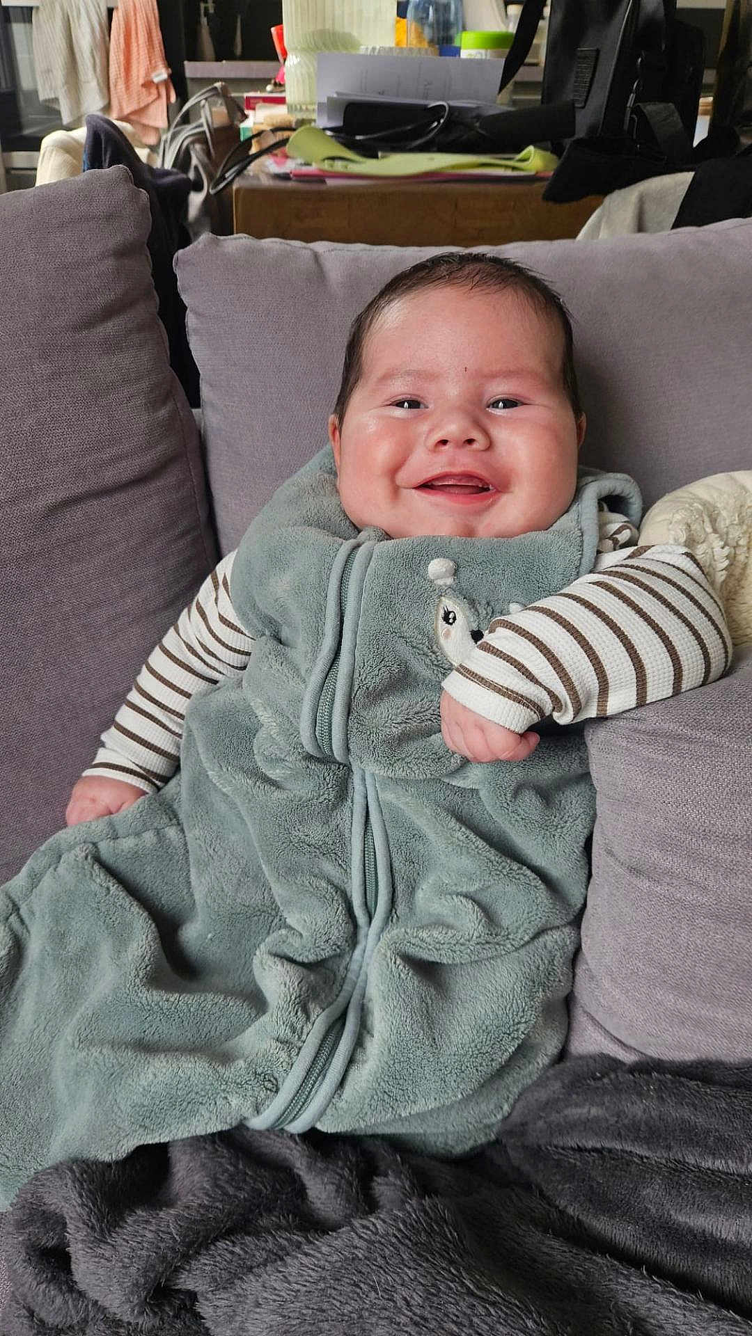 Aimé participe au concours pour gagner de l'argent avec cette photo : baby, blanket, chubby_cheeks, couch, cozy, furniture, hand, happy, home_interior, infant, living_room, pajamas, pillow, plush, portrait, seated, smile, soft_texture, striped_sleeves, zipper
