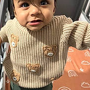 Zain is registered to the contest to win money with this photo: toddler, child, sweater, knitted, teddy_bear, crib, mattress, rainbow_pattern, sun_pattern, curious, indoor, person, clothing, baby, cute, standing, close_up, face, hair, foot