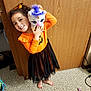Jemma joined the competition — help win amazing prizes! child, girl, halloween_costume, orange_shirt, black_skirt, barefoot, plush_toy, unicorn, smiling, indoor, carpet, wooden_door, long_sleeves, hair_bow, cute, happy, playful, toy, decor, portrait