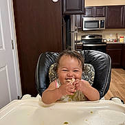 Daniella joined the competition — help win amazing prizes! baby, bib, cabinet, cute, eating, face, flooring, food, furniture, happy, high_chair, indoor, infant, kitchen, microwave, oven, person, smiling, stainless_steel, wood_floor