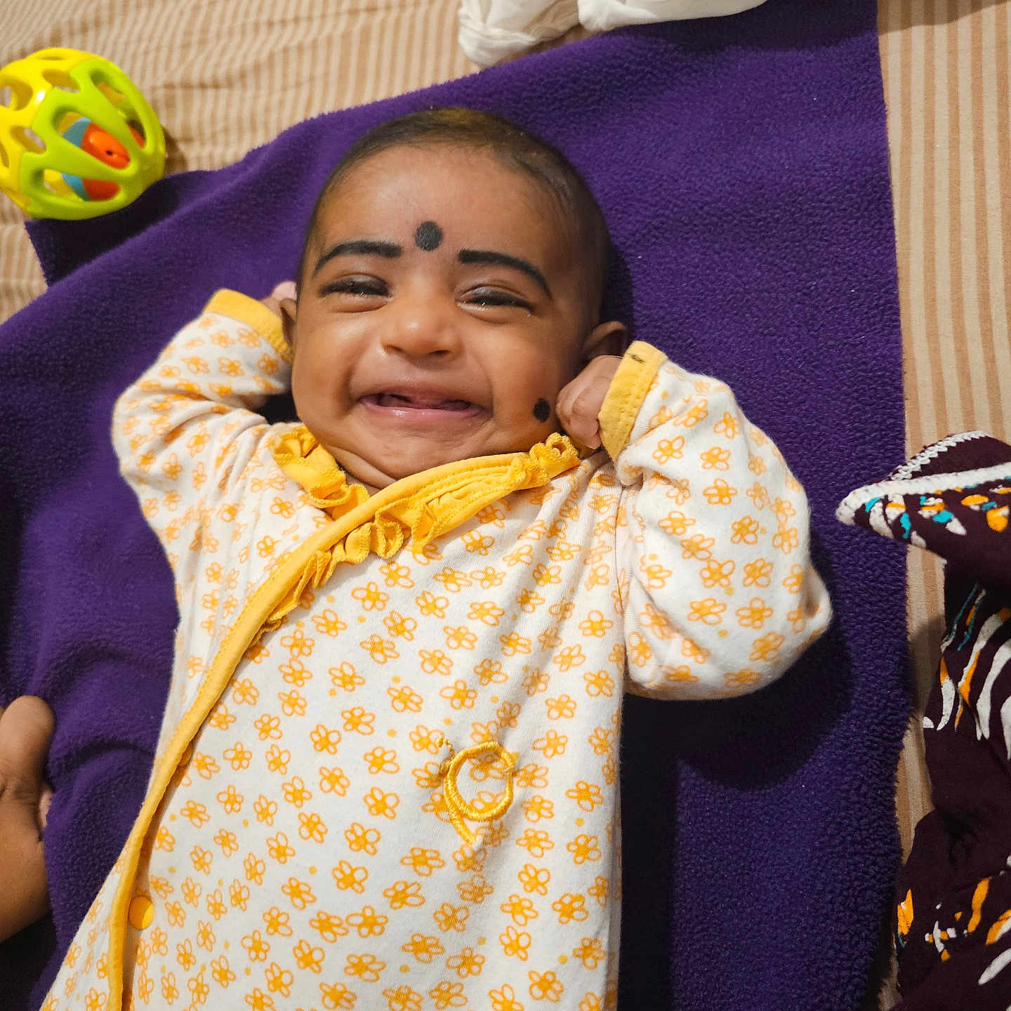 Shivani joined the competition — help win amazing prizes! baby, bed, cheerful, child, comfort, cute, expression, face, happy, indoor, infant, lying_down, onesie, person, purple_blanket, skin, small_child, smiling, toy_ball, yellow_clothing