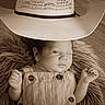baby, infant, winking, cowboy_hat, sepia_tone, fur_blanket, wooden_floor, portrait, cute, child, hat, clothing, smile, hand, face, newborn, lying_down, one_eye_closed, adorable, cozy