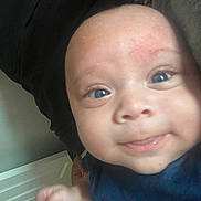 Kevin joined the competition — help win amazing prizes! baby, face, blue_eyes, smile, close_up, infant, person, skin, hand, clothing, dark_background, indoor, portrait, cute, young_child, head, expression, looking_at_camera, human, child