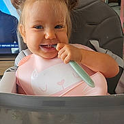 Lucia participe au concours pour gagner de l'argent avec cette photo : toddler, child, smiling, high_chair, bib, spoon, hair_buns, indoor, feeding, cute, happy, face, baby, clothing, table, toy_figures, person, seat, pink, blue_eyes