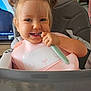 toddler, child, smiling, high_chair, bib, spoon, hair_buns, indoor, feeding, cute, happy, face, baby, clothing, table, toy_figures, person, seat, pink, blue_eyes