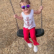Brynnslee is registered to the contest to win money with this photo: casual, chain, child, cute, footwear, fun, happy, heart_shaped_sunglasses, outdoor, person, play, playground, portrait, red_pants, smiling, summer_clothing, sunlight, swing, white_tank_top, wood_chips