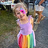 child, girl, face_paint, smiling, rainbow_skirt, purple_top, outdoor, grass, pavement, truck, adult, event, sunset, person, happy, casual_clothing, shoes, people, portrait, fun