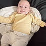baby, infant, child, yellow_clothing, white_pants, dots, blanket, cushion, black_background, smiling, tongue_out, laying_down, cute, happy, indoors, person, head, face, arms_out, soft_toys