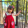 Alea joined the competition — help win amazing prizes! toddler, child, girl, red_dress, strawberry, hair_bow, outdoor, porch, railing, wooden_floor, smiling, cute, curly_hair, short_sleeves, natural_light, daytime, standing, person, fashion, greenery