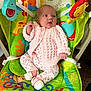 animal_print, baby, baby_rocker, carpet, child, colorful, comfortable, curious, cute, doll, floral_pants, indoor, infant, knitted_clothing, looking_away, pink_sweater, seated, small_hands, toys, white_socks