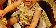 Maverick is registered to the contest to win money with this photo: toddler, child, high_chair, fork, food, smiling, indoor, floor_tiles, wooden_chair, person, hand, foot, shirt, table, happy, baby, seat, cute, playful, skin