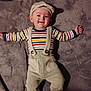 baby, child, smile, striped_shirt, overalls, hat, blanket, soft_texture, lying_down, happy, infant, indoors, cute, face, headwear, clothing, person, baby_clothes, socks, portrait