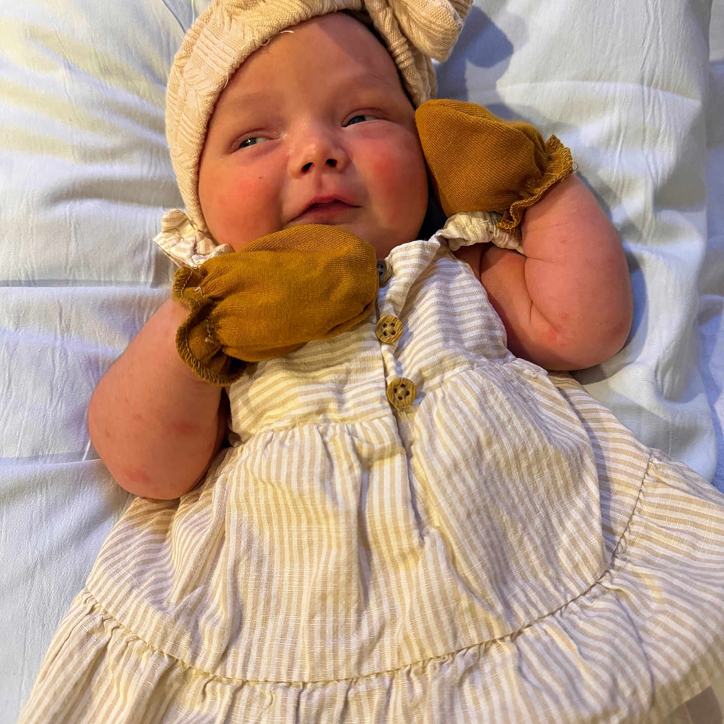 Paisley is registered to the contest to win money with this photo: baby, infant, child, mittens, headband, bow, dress, striped_clothing, lying_down, white_sheet, cute, chubby_cheeks, small_hands, soft_lighting, indoors, portrait, closeup, skin, expression, person