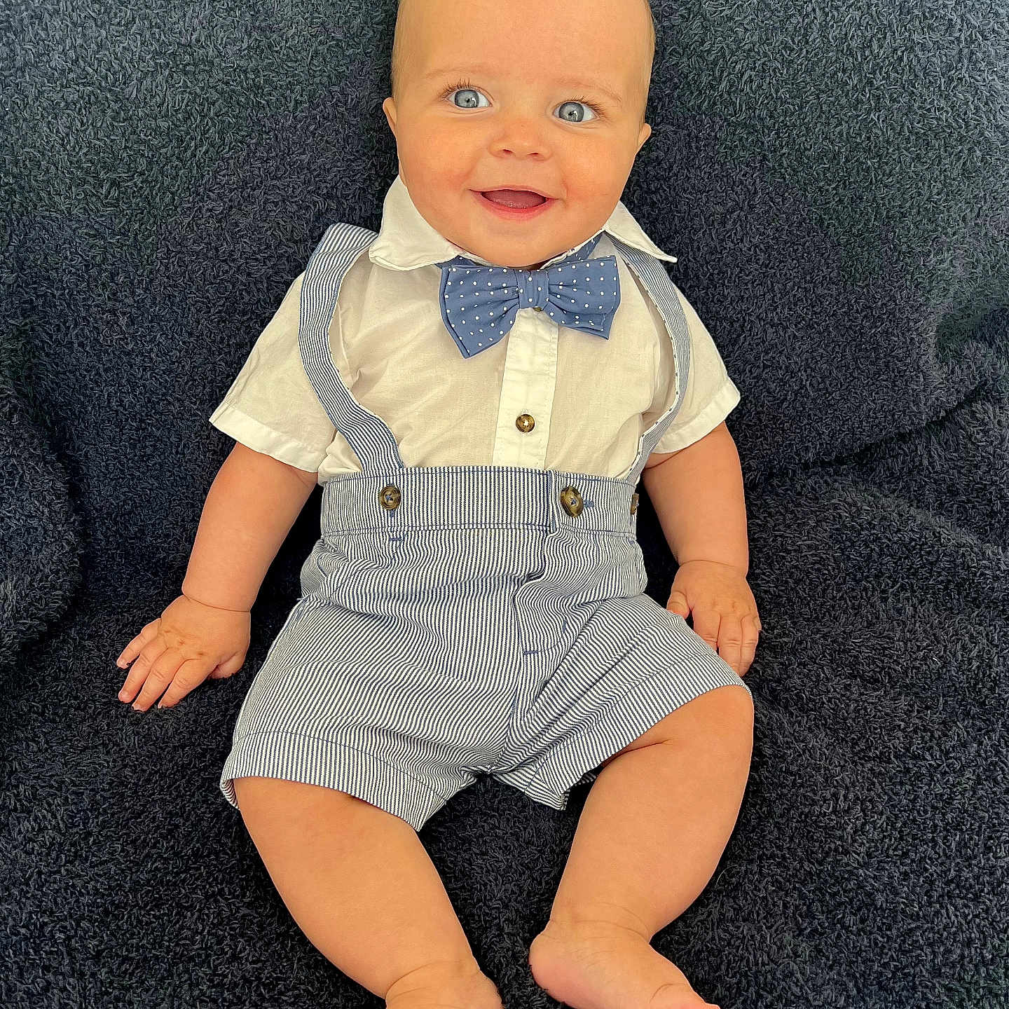 Luke is registered to the contest to win money with this photo: accessories, baby, bowtie, clothing, couch, face, formalwear, furniture, happy, head, jeans, pants, person, photography, portrait, shirt, sitting, suit, suspenders, tie