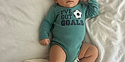 Vincent joined the competition — help win amazing prizes! baby, infant, onesie, text_on_clothing, soccer_ball_graphic, blanket, bed, white_bed_sheet, soft_texture, lying_down, child, skin, face, legs, arms, foot, hand, casual_clothing, indoor, calm_expression