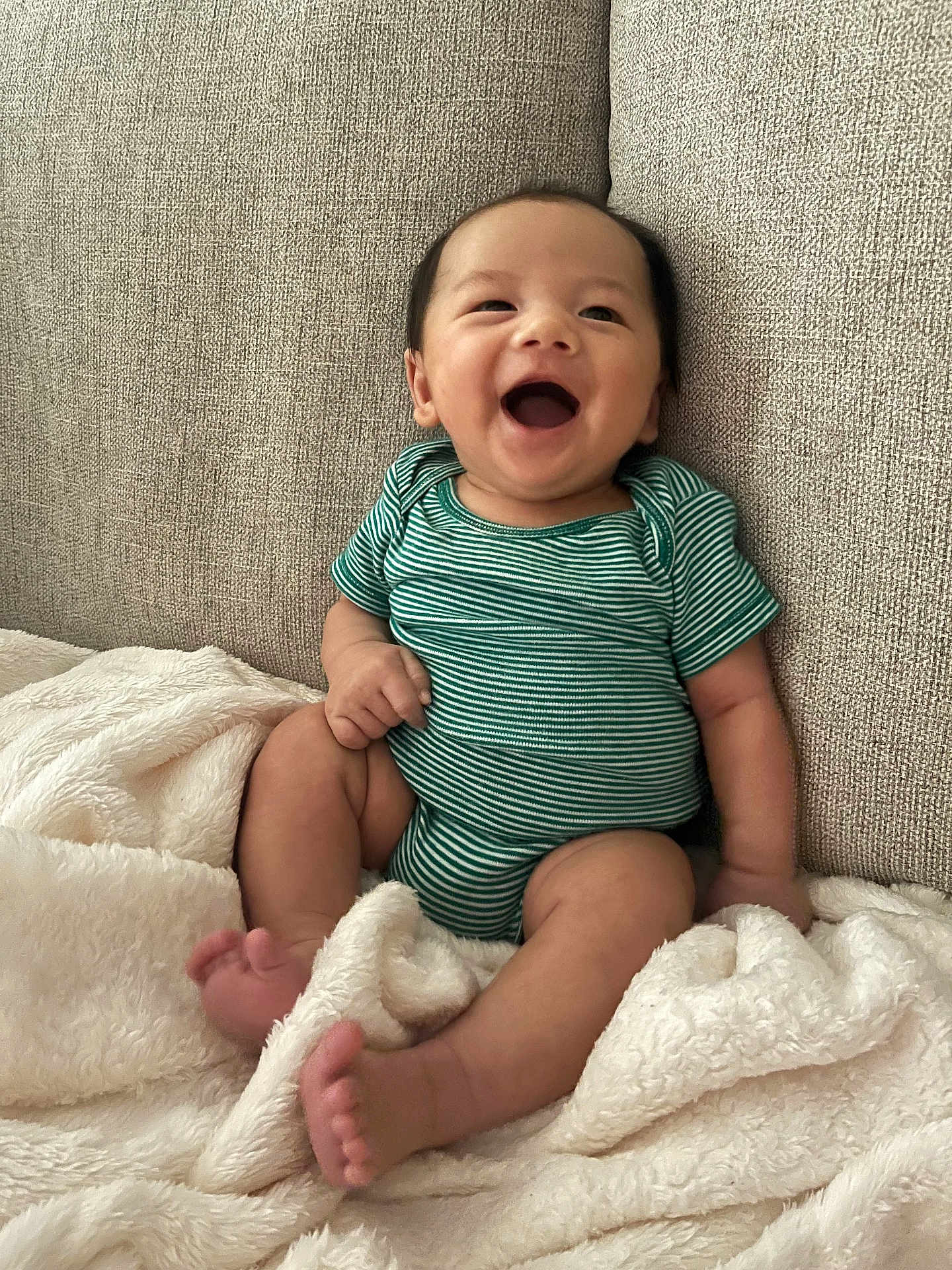 Vincent joined the competition — help win amazing prizes! baby, child, infant, smiling, laughing, onesie, striped_clothing, blanket, couch, fabric, soft_texture, happy, cute, indoors, seated, person, face, skin, foot, hand