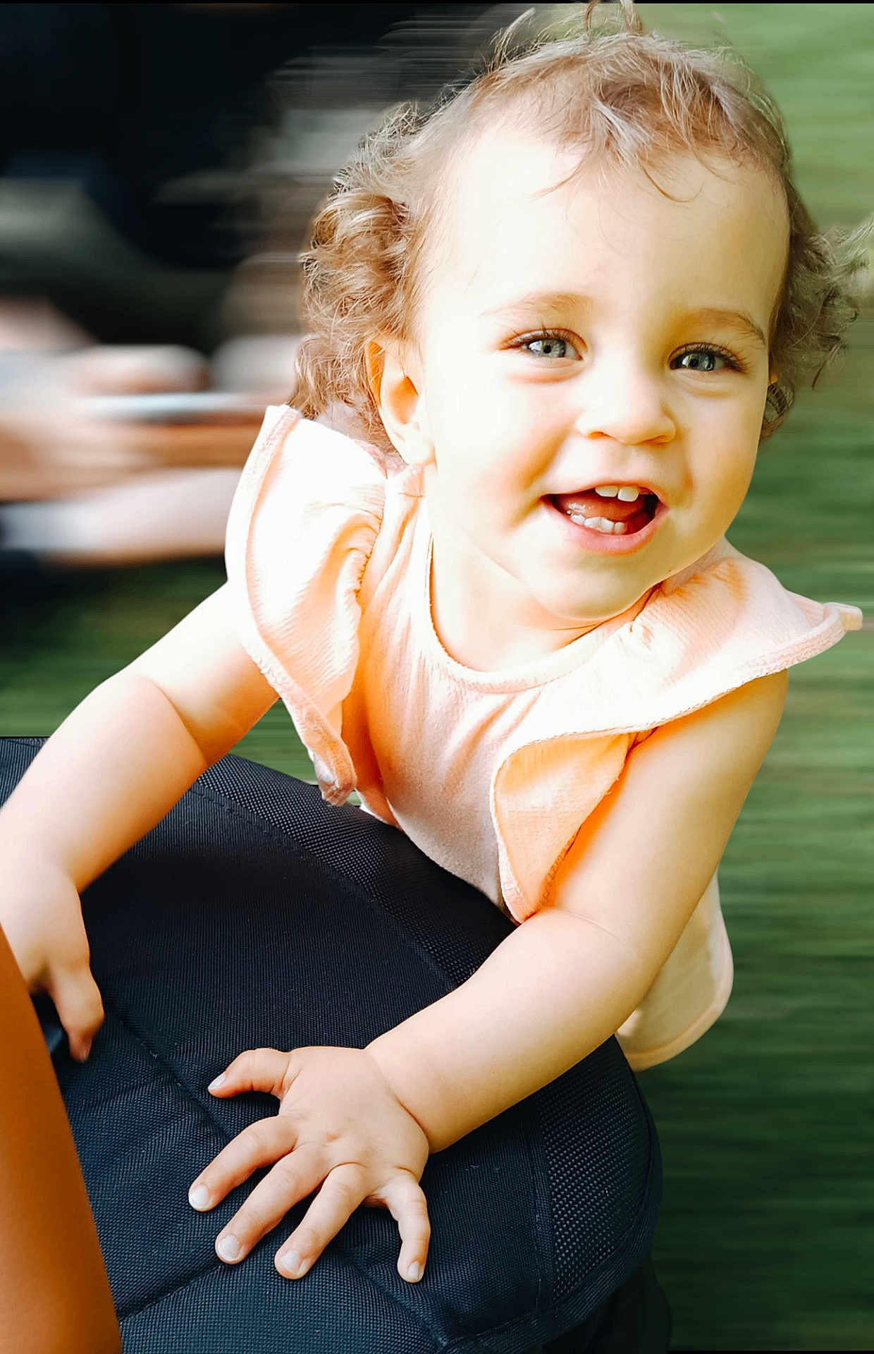 Emelia participe au concours pour gagner de l'argent avec cette photo : child, toddler, smile, curly_hair, peach_outfit, happy, face, hand, chair, black_chair, indoors, portrait, cute, baby, young_child, person, skin, eyes, expression, close_up